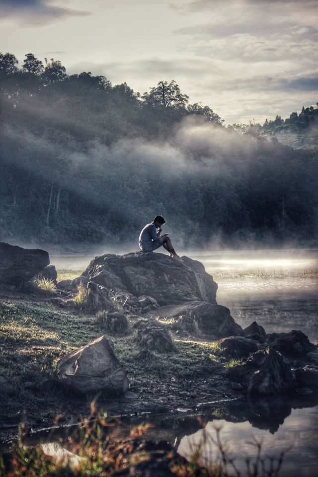 Person sitting alone beside a misty lake reflecting on Stoic philosophy and inner peace.